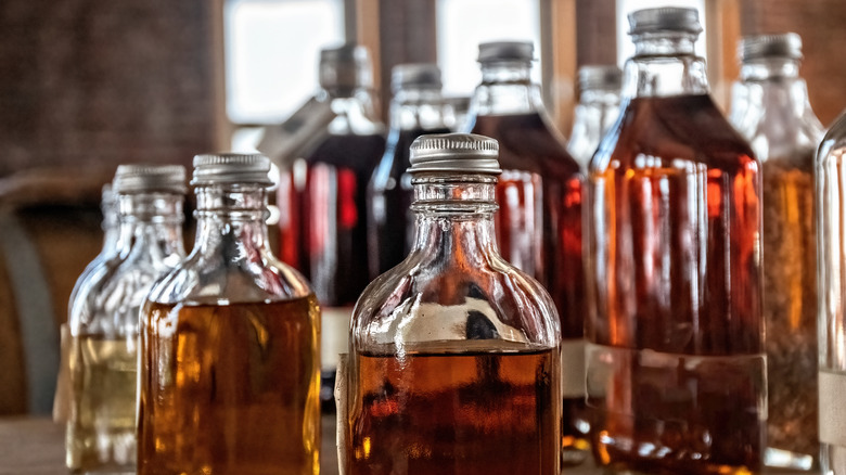 Rows of small, unlabeled bottles of bourbon, some close up, some from a distance on a rustic wooden countertop.