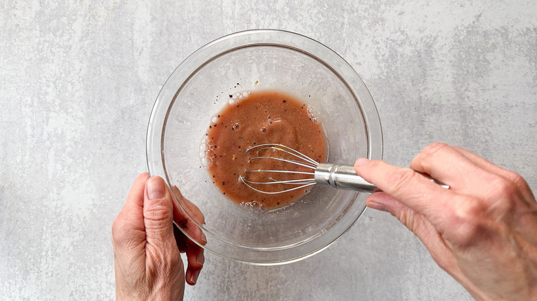 Whisking together ingredients for vinaigrette dressing in glass bowl