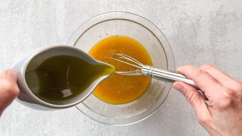 Whisking olive oil into salad dressing in glass bowl