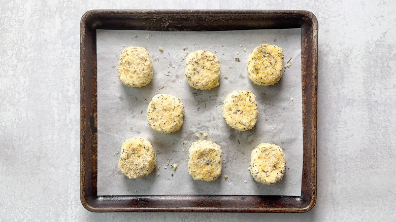 Breaded goat cheese rounds ready to bake on parchment-lined baking sheet