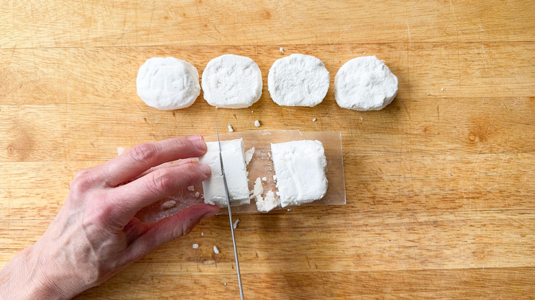 Cutting goat cheese log into rounds on cutting board