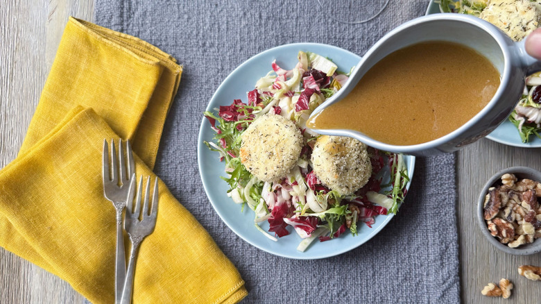 Pouring dressing on breaded and baked goat cheese salad
