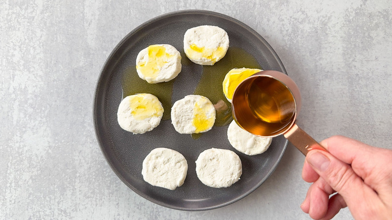 Drizzling olive oil over goat cheese rounds on plate with measuring cup
