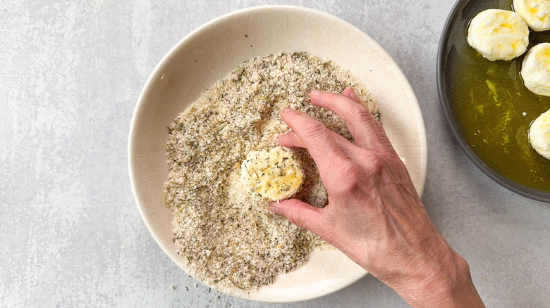 Coating goat cheese rounds with olive oil in breading mixture in bowl