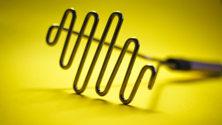 Metal handheld potato masher against a yellow background