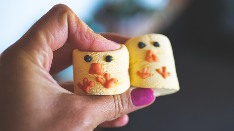 A person's hand holds marshmallows that have been decorated to look like yellow chicks.
