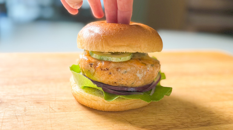 Broiled salmon burger with curry remoulade and brioche bun on cutting board