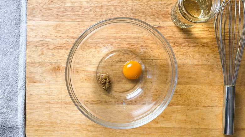 Egg yolk, vinegar, and whole grain mustard in glass bowl with whisk and oil