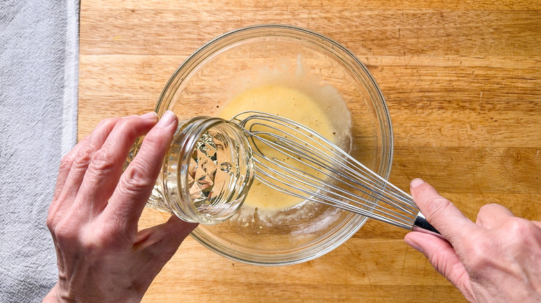 Adding oil to remoulade sauce in glass bowl with a whisk