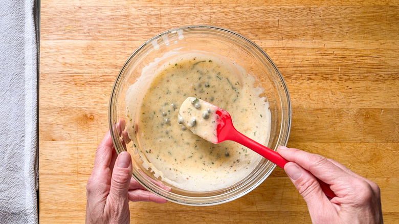 Stirring curry remoulade sauce in glass bowl with spatula on cutting board