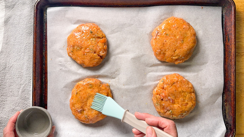 Brushing salmon burgers with olive oil using pastry brush on baking sheet