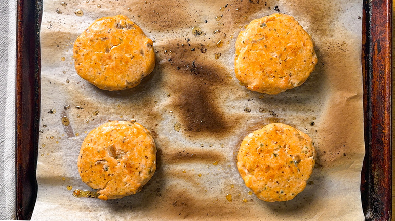 Broiled salmon burgers on charred parchment paper on baking sheet