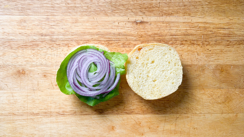 Burger bun on cutting board with lettuce and red onion slices