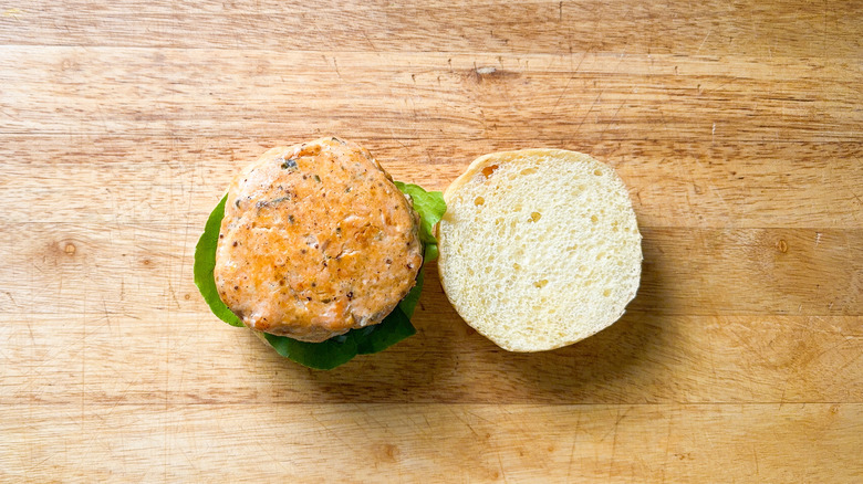 Broiled salmon burger on top of onion and lettuce on bun