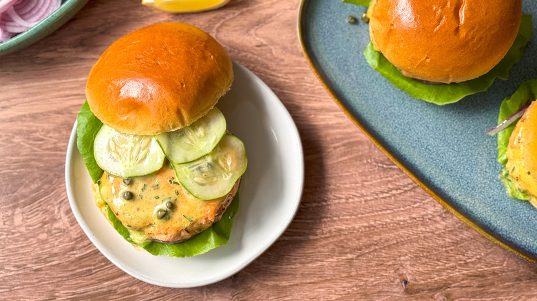 Broiled salmon burger with curry remoulade on brioche bun with lettuce and onion on cutting board