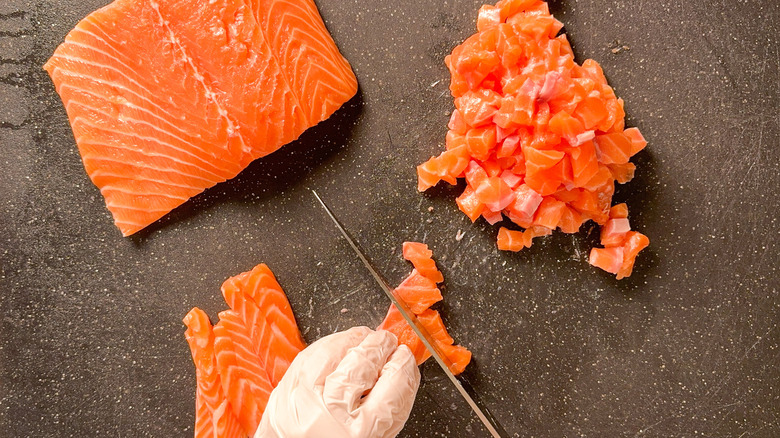 Cutting salmon filets into cubes with knife on cutting board