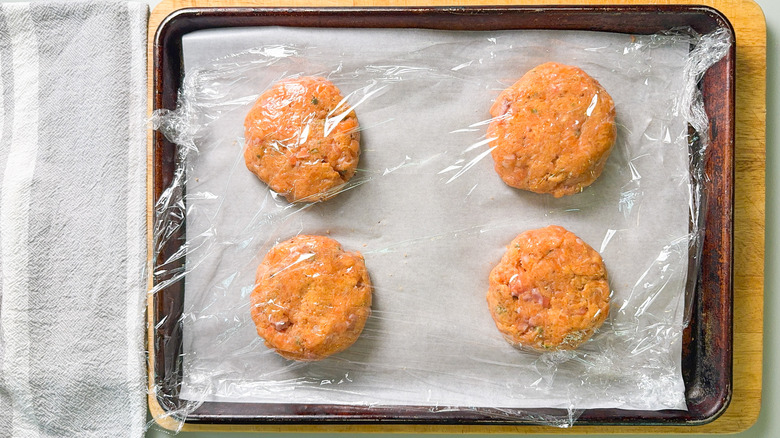 Salmon patties on parchment paper on baking sheet covered with plastic wrap