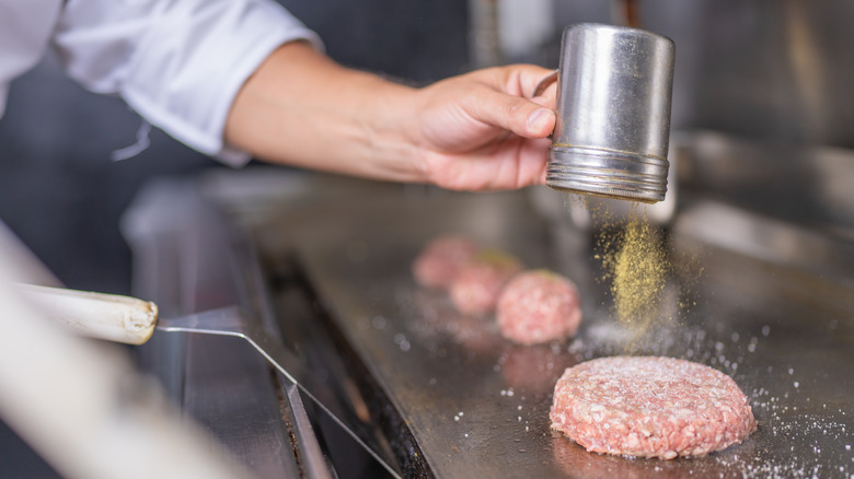 chef seasoning burger while cooking