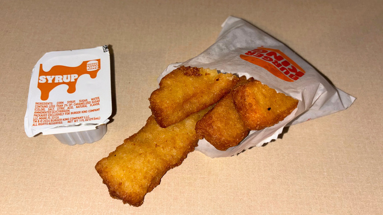 French toast sticks and syrup pouring out of a paper bag on a countertop.