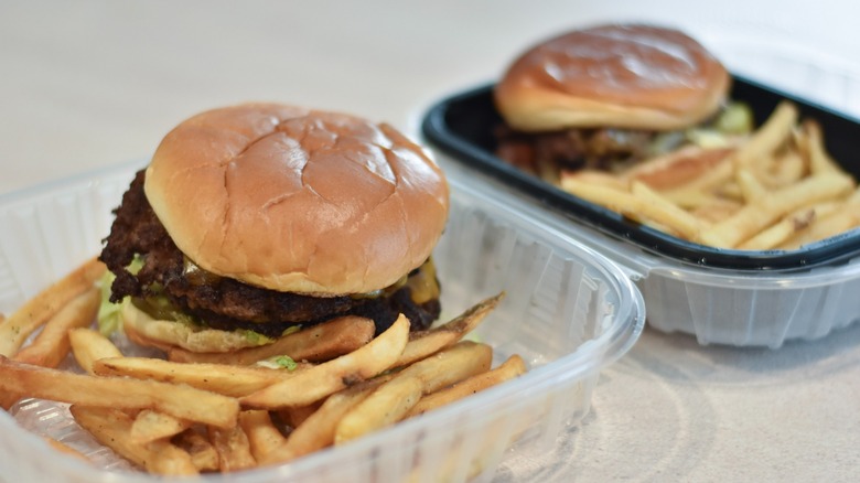 Two burgers in containers with fries on a white countertop
