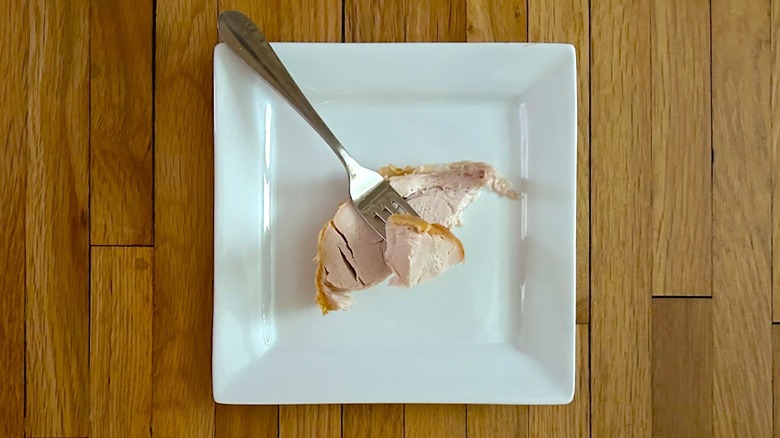 Slice and bit of turkey breast on a fork on a white, square plate