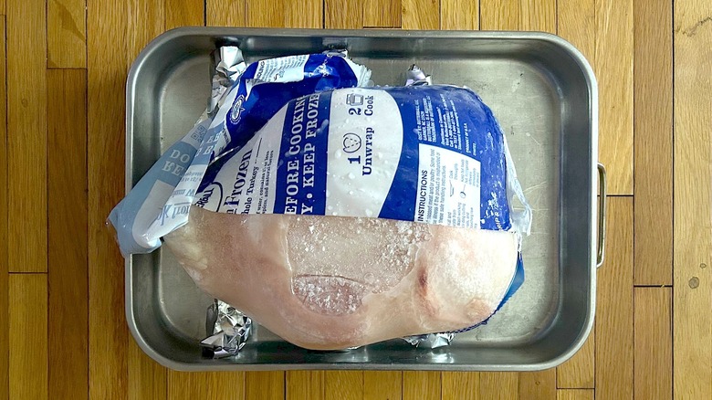 Partially unwrapped whole frozen turkey in a roasting pan