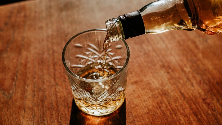 Pouring bourbon into rocks glass on wood table