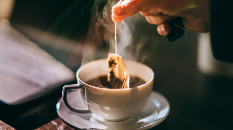 An individual picking a tea bag out of a cup.