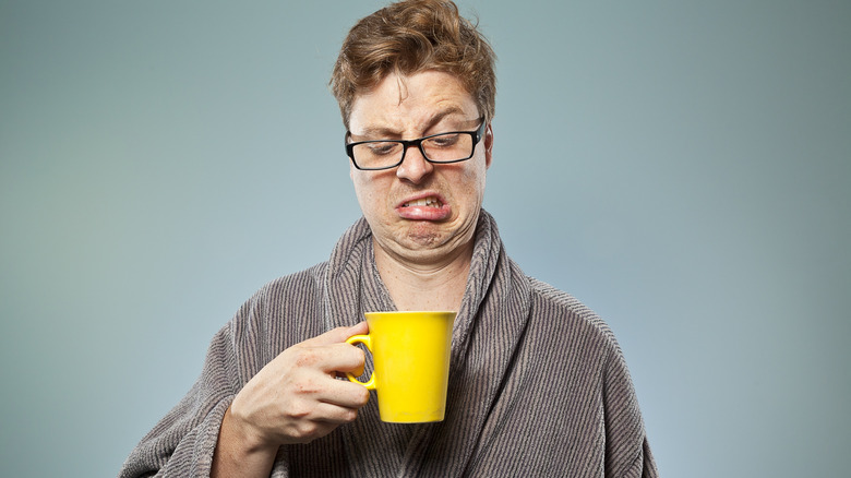 A man frowning while holding a cup of tea.