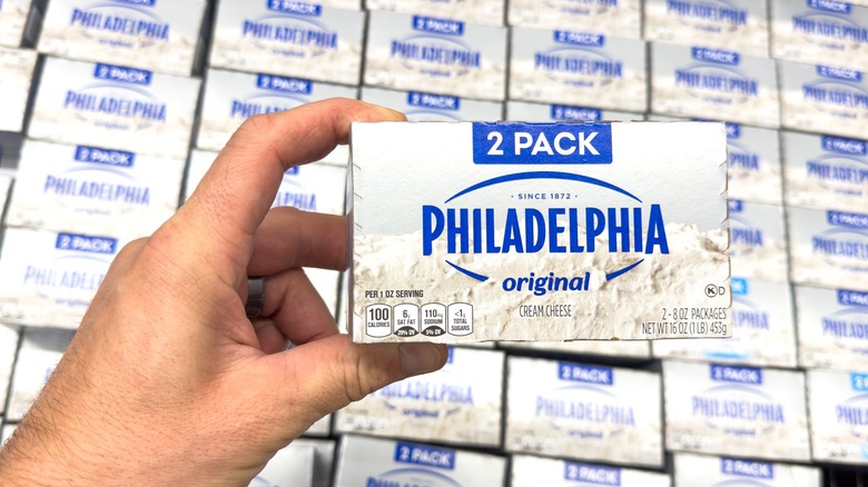 Hand holding Philadelphia in front of stacks of cream cheese at the grocery store