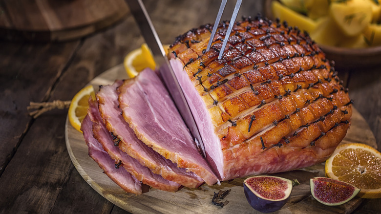 Slicing a glazed holiday ham dotted with cloves