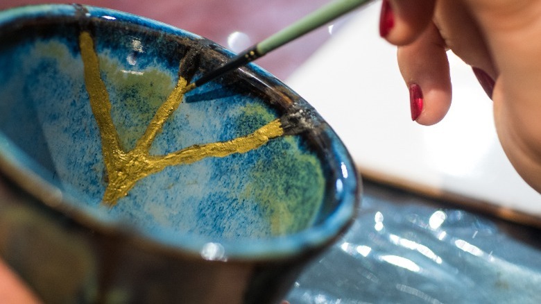 hand brushing gold paint onto a repaired ceramic cup