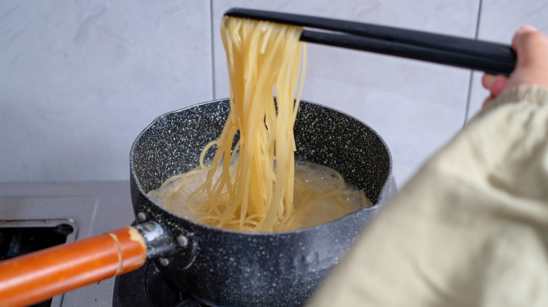 Someone cooking spaghetti and taking out the noodles to test them