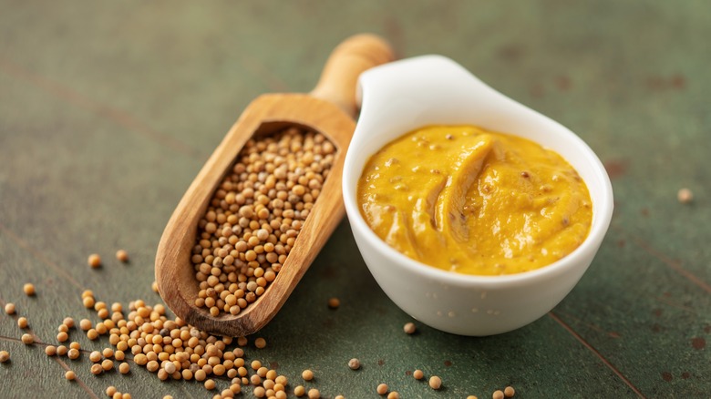 Mustard in a bowl next to a scoop full of mustard seeds