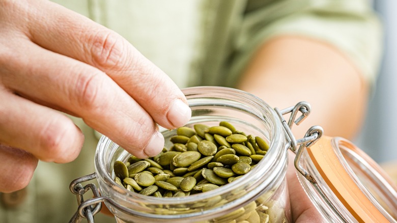 Hand pinching pepitas out of a canister