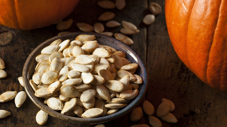 Pumpkin seeds in a bowl surrounded by pumpkins