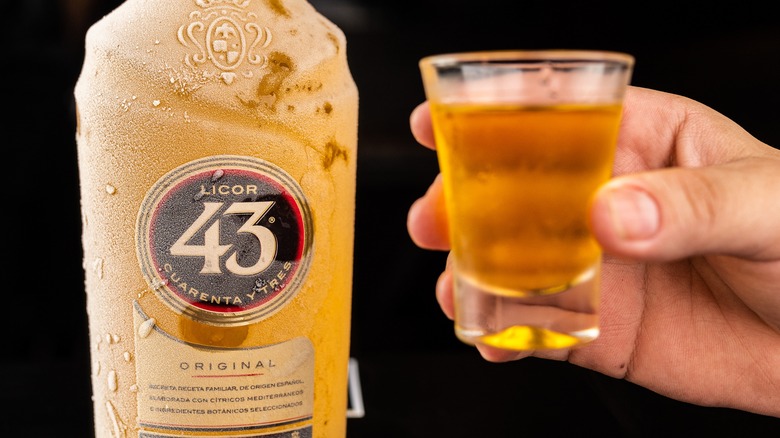 An icy bottle of Licor 43 with a person holding a shot
