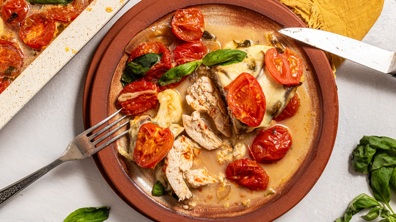 Cheesy caprese chicken bake sliced on a plate with roasted tomatoes