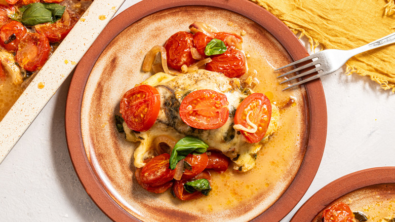 Plate with caprese chicken bake and roasted cherry tomatoes on top, fork on the side
