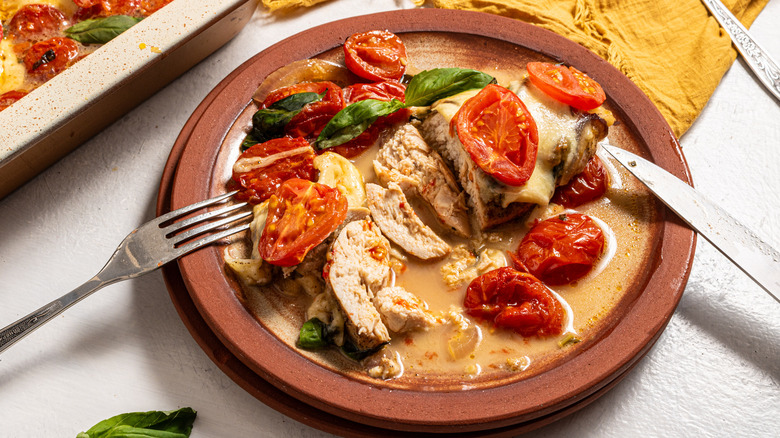 Plate with caprese chicken bake sliced with roasted cherry tomatoes and fresh basil