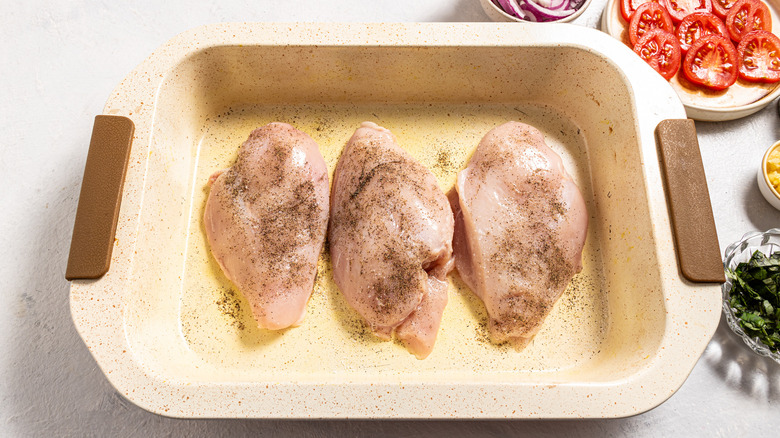 Baking dish with three chicken breasts seasoned with salt and black pepper