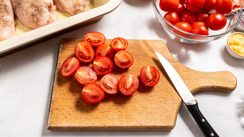 Sliced cherry tomatoes on a cutting board with a knife