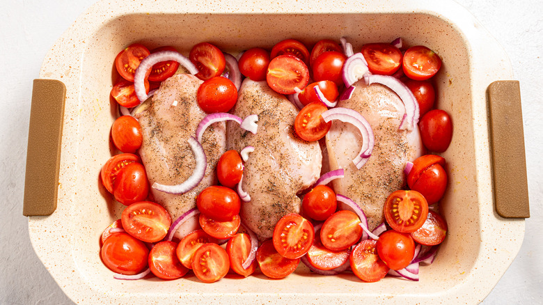 Baking dish with chicken breast, sliced cherry tomatoes, and red onion