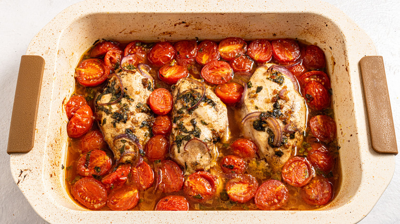 Baking dish with roasted chicken breasts, cherry tomatoes, and herbs in a sauce