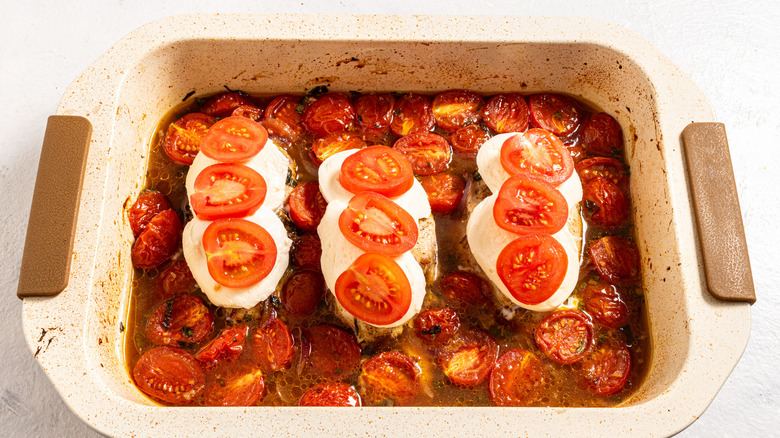 Baking dish with chicken breasts in a cherry tomato sauce covered with fresh mozzarella and cherry tomato slices