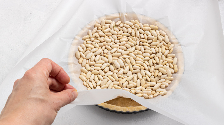 Placing a parchment paper with beans over a pie crust