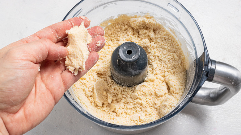 Hand checking the consistency of a dough from a food processor