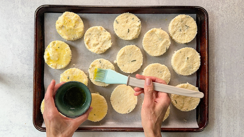 Brushing cheesy truffled grit cakes on sheet pan with truffle oil using pastry brush