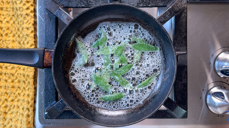 Sage leaves cooking in melted butter in skillet on stovetop