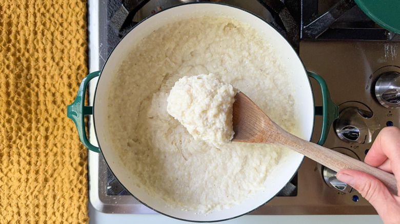 Wooden spoon filled with cooked grits over pot on stovetop